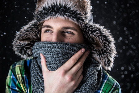 Closeup portrait of a pensive man in hat and scarf with snow on background