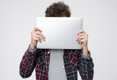 Young man covering face with laptop over gray backgroundの写真素材