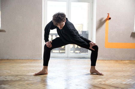Young male dancer stretching at gym
