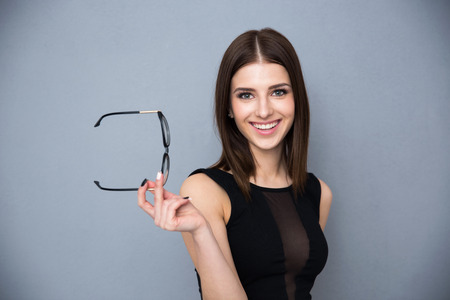 Portrait of a smiling cute woman holding glasses over gray background. Wearing in black sexy dress. Looking at the camera.の写真素材