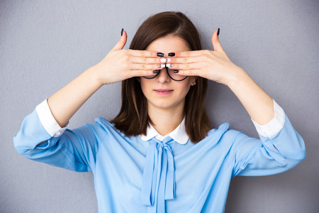 Businesswoman covering her eyes over gray background. Wearing in blue shirtの写真素材