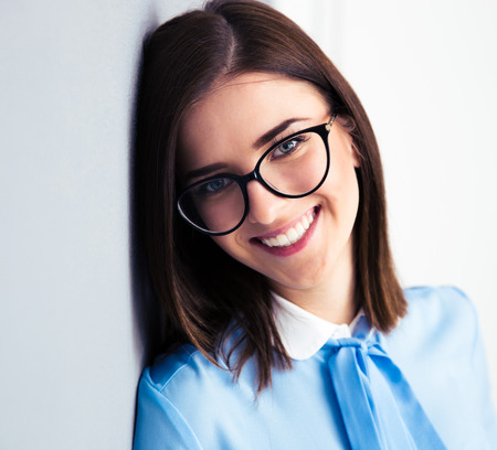 Portrait of a smiling young businesswoman in glasses leaning on the gray wall. Looking at camera. Wearing in blue shirtの写真素材