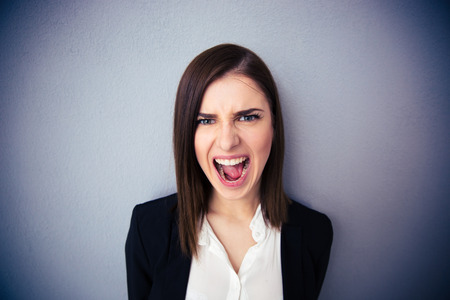 Angry businesswoman shouting over gray background. Looking at cameraの写真素材