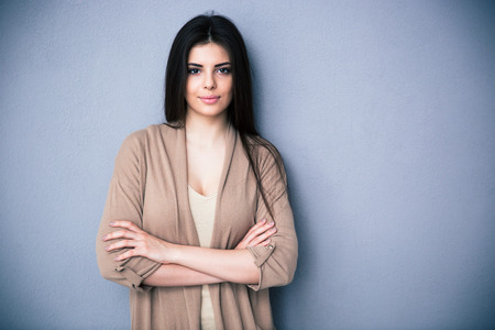 Portrait of attractive young woman with arms folded standing over gray background. Looking at cameraの写真素材