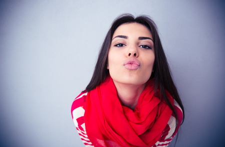 Cute woman kissing at camera over gray background. Wearing in pink scarf and sweater.の写真素材