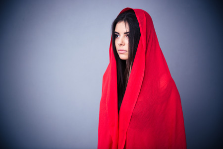 Portrait of a beautiful woman in red cloth looking away. Standing over gray background.の写真素材