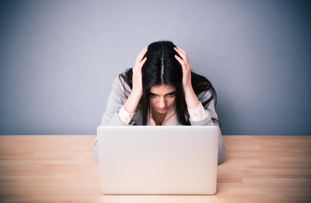 Tired businesswoman sitting at the table over gray background. Looking on laptopの写真素材