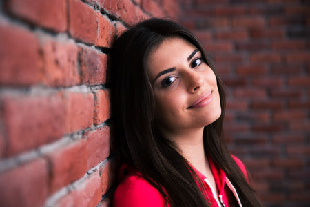 Closeup portrait of a happy woman leaning on the brick wallの写真素材