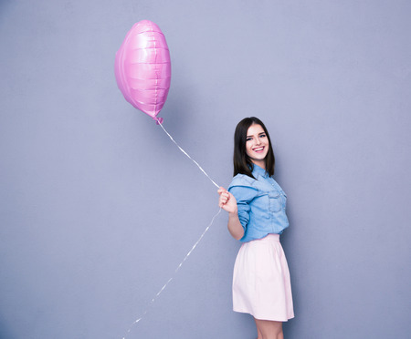 Cheerful woman holding balloon and looking at camera over gray background. Wearing in shirt and skirtの写真素材