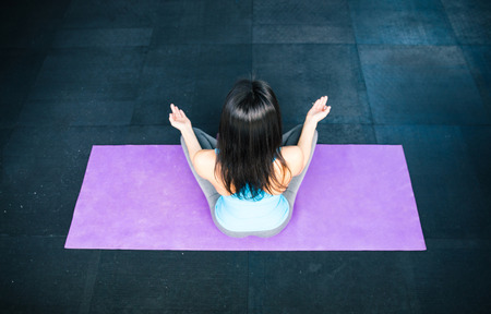 Back view portrait of a woman meditating on yoha mat at gym