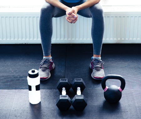 Closeup image of a woman sitting at gym with dumbbells, shaker and weightの写真素材