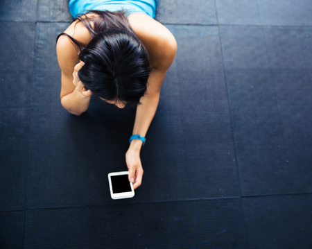 Fit woman lying on the floor with smartphoneの写真素材