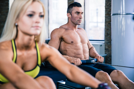 Handsome man and beautiful woman doing exercises on training simulator in crossfit gym. Focus on manの写真素材