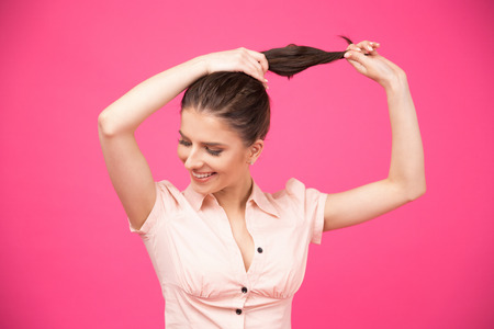 Happy young woman making her hair over pink background.の写真素材