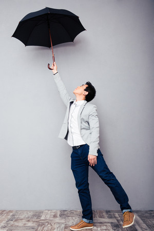 Full length portrait of a young man holding umbrella over gray wallの写真素材