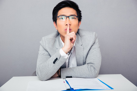 Asian businessman in glasses showing finger over lips and looking at camera. Be quiet!!!の写真素材