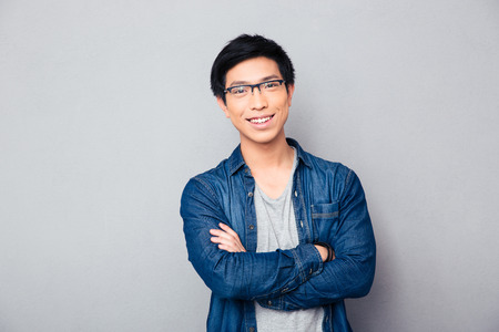 Portrait of a happy asian man with arms folded over gray background. Looking at cameraの写真素材