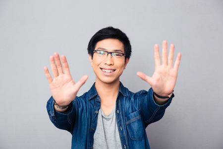 Happy asian man in glasses making stop gesture with palm over gray backgroundの写真素材
