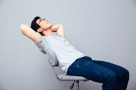Pensive man relaxing on the chair over gray background. Looking upの写真素材