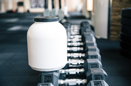 Closeup image of a plastic container with sports nutrition on dumbbells in gymの写真素材