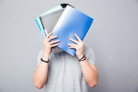 Man covering his face with folders over gray backgroundの写真素材