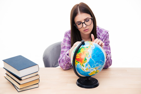 Pensive young female student sitting at the table with globe over white backgroundの写真素材