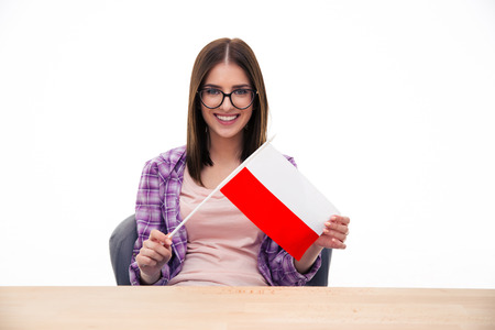 Young woman sitting at the table and holding Polish flag over white background and looking at cameraの写真素材