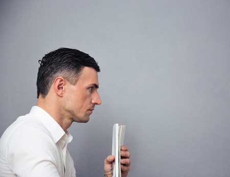 Pensive businessman holding newspaper over gray backgroundの写真素材