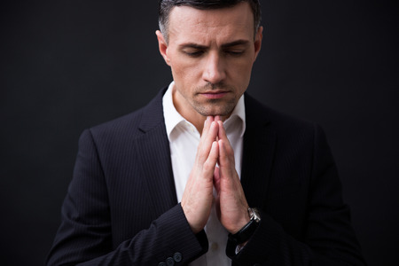 Portrait of a businessman in formal wear praying over black backgroundの写真素材