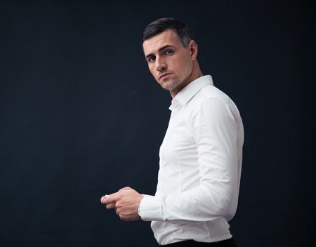 Serious businessman using smartphone and looking at camera over black background