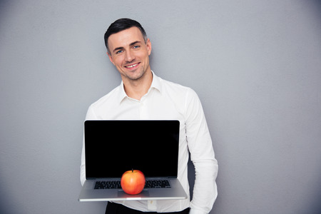 Happy businessman showing blank laptop screen over gray background. Looking at cameraの写真素材