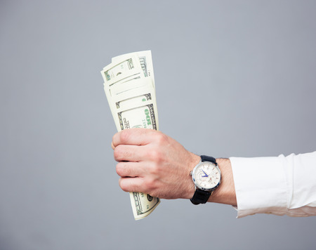 Closeup image of a businessman hand holding bills of US dollar over gray background