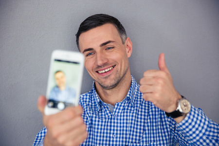 Happy man showing thumb up and making selfie photo on smartphoneの写真素材