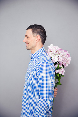 Side view portrait of a happy man hiding flower behind his backの写真素材
