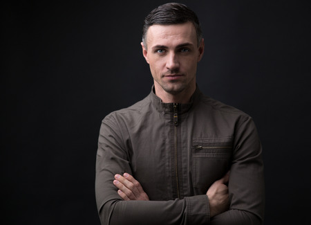 Portrait of a happy man standing with arms folded over black background and looking at cameraの写真素材