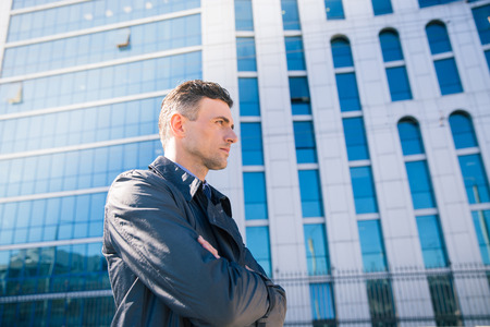 Side view portrait of a businessman standing with arms folded outdoors. Glass building on backgroundの写真素材
