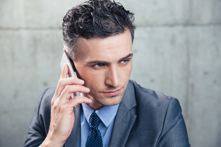 Closeup portrait of a confident businessman talking on the phone and looking away over concrete wallの写真素材