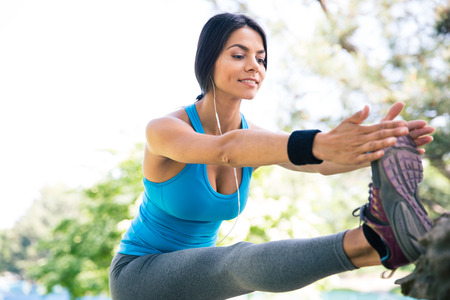 Sporty happy woman stretching legs outdoors in park
