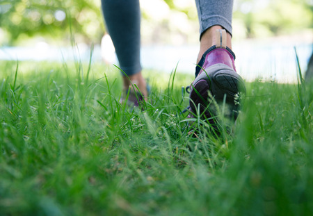 Closeup image of a sports footwear on female feet running on green grassの写真素材
