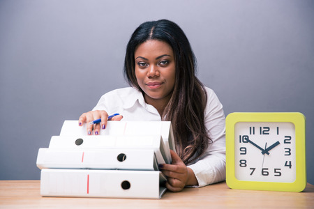 African businesswoman sitting at the table with pen and folders over gray background. Looking at cameraの写真素材