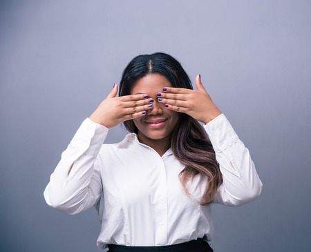 Happy african businesswoman covering her eyes over gray backgroundの写真素材
