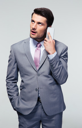 Bored businessman talking on the phone over gray backgroundの写真素材