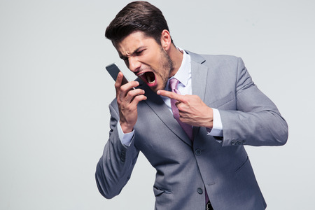 Angry businessman shouting on the phone over gray backgroundの写真素材