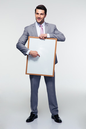 Full length portrait of a happy businessman holding blank board over gray background. Looking at cameraの写真素材
