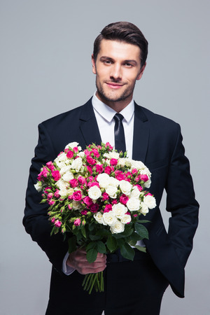 Handsome businessman holding flowers over gray background and looking at cameraの写真素材