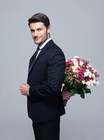 Businessman hiding bouquet of flowers behind his back over gray background and looking at cameraの写真素材