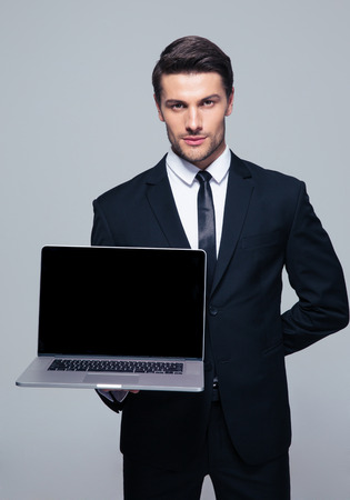Confident businessman showing blank laptop screen over gray background. Looking at cameraの写真素材