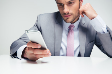 Confident businessman sitting at the table and using smartphone over gray background. Focus on smartphoneの写真素材
