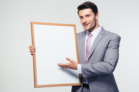 Smiling businessman holding blank board over gray background. Looking at cameraの写真素材