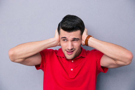Casual handsome man covering his ears with hands over gray background and looking awayの写真素材